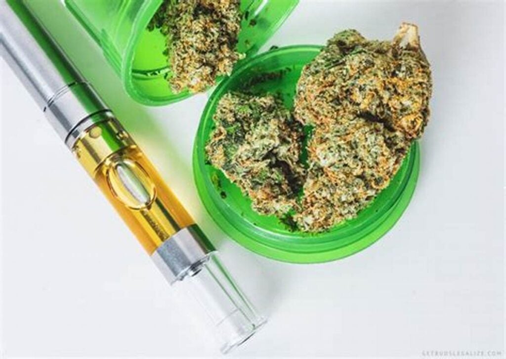 Cannabis vape cartridge next to dense Soul Shine strain buds in a green grinder on a white background, illustrating consumption methods for THC-rich hybrid strains.